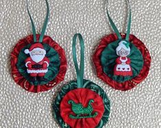 two christmas ornaments with santa clause on top and green trim around the edges, hanging from strings