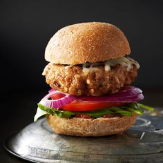 a chicken sandwich with lettuce, tomato and onion on a bun sitting on a metal tray