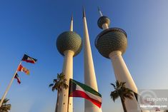 three tall towers with flags flying in the air next to palm trees and a blue sky