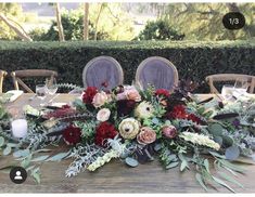 an arrangement of flowers and greenery is displayed on a wooden table with purple chairs