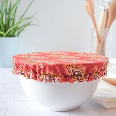 a white bowl with a red cover on top of it next to a potted plant