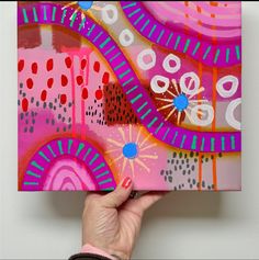 a person holding up a colorful painting on a white wall with pink and blue designs