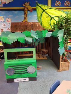 a green truck made out of cardboard sitting in front of a jungle tent with trees and giraffes on it