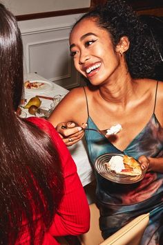 two women sitting at a table with food in their hands and one is eating something