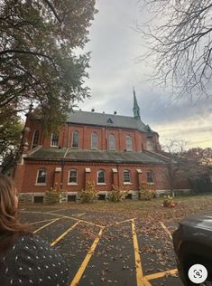 a woman standing in front of a red brick building with a steeple on top