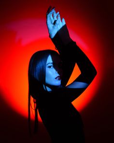 a woman in black shirt holding her hand up to the side with red light behind her