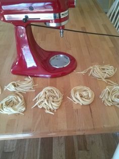 pasta being made in a red mixer on top of a wooden table