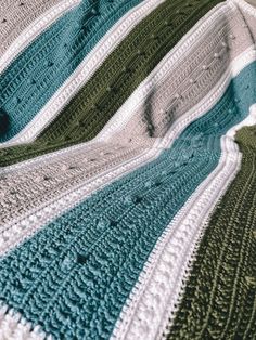 a crocheted blanket sitting on top of a bed covered in green and white blankets