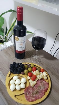 a wooden plate topped with meat, cheese and vegetables next to a bottle of wine