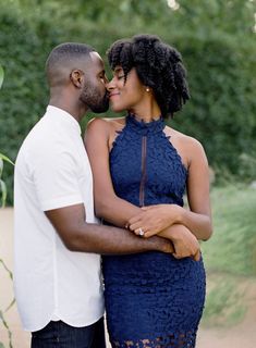 a man and woman standing next to each other in front of some trees with their arms around each other