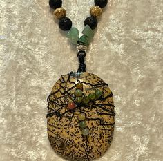 Dendritic Picture Jasper cabochon wrapped in black wire with India and Moss Agate added to the wrap. The cabochon is 2 1/8" long and 1 1/2" wide. Huge!  A mix of Aventurine, Black Lava, Carnelian and Silver alloy beads on 1mm genuine black leather cording for the longer pendant necklace at 30". The shorter one is bronze leather cord at 22" with Picture Jasper, Black Lava, Carnelian and Silver Alloy beads . These are joined together with silver wire and a silver toggle for closure.  No nickel or lead used. Please use the Last On, First Off approach. Stones discolor with lotions, perfumes, hairspray, sweat, chlorine, even some soaps, and will break if dropped. Leather Beaded Necklace, Boho Retro, Long Pendant Necklace, Jasper Pendant, Picture Jasper, Long Pendant, Bead Leather, Moss Agate, Multi Strand