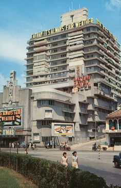 people walking in front of a tall building on the corner of a street with cars driving by