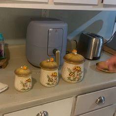 the kitchen counter has three ceramic pots and a toaster on it, along with other items