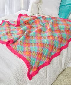 a bed topped with a colorful blanket next to a white stuffed animal on top of it