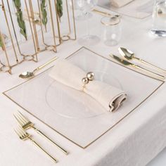 a white table with gold place settings and napkins on it, along with silverware