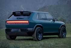 the rear end of a blue suv parked in a field with mountains in the background