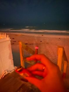 a hand is holding a lit candle on the beach at night, with an ocean in the background