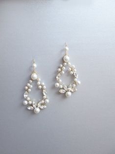 two pairs of pearl and crystal earrings on top of a white surface with an object in the background