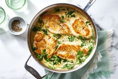 a pan filled with chicken and spinach on top of a table next to glasses