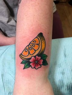 an orange slice tattoo on the arm with flowers and leaves around it, sitting on a person's leg