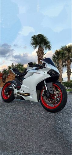 a white motorcycle parked on top of a parking lot next to trees and palm trees