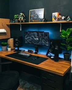 a desk with a computer, speakers and plants on it in front of a blue wall