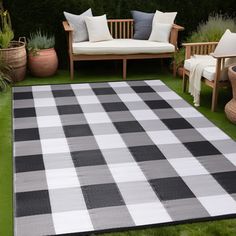 a black and white checkered rug sitting on top of a grass covered field next to wooden benches