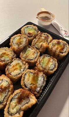 a tray filled with sushi next to a cup of coffee on top of a table