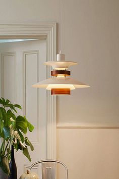 three lights hanging from a ceiling over a table with two vases and a potted plant