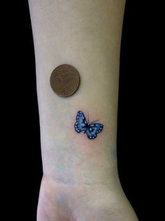 a small blue butterfly tattoo on the left inner forearm and wrist, next to a penny