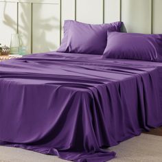 a bed covered in purple sheets and pillows