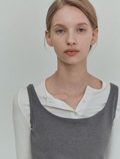 a woman with blue eyes wearing a grey and white top, standing in front of a white wall