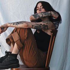 a woman sitting on top of a wooden chair with tattoos on her arms and legs