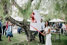 a bride and groom standing next to a wedding cake in the middle of a park