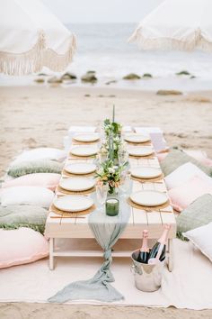 a table set up on the beach with plates and drinks