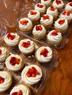 cupcakes with white frosting and strawberries on top in plastic trays