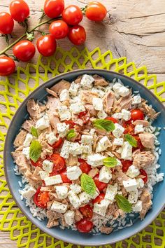 a blue bowl filled with chicken, tomatoes and feta cheese on top of a yellow mat