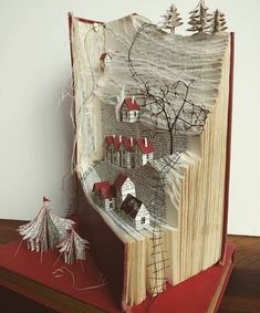 an open book with paper houses and trees on it, sitting on top of a wooden table