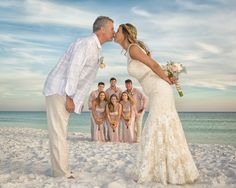 a bride and groom kissing on the beach with their wedding party