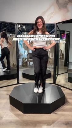 a woman standing on top of a black platform in front of mirrors with her hands on her hips