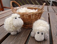 two stuffed sheep sitting on top of a wooden table next to a wicker basket