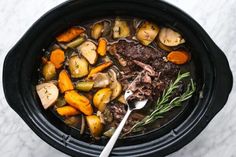 a crock pot filled with meat and vegetables on top of a marble countertop