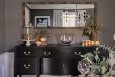 a black dresser with gold accents and vases on it, in front of a mirror