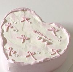 a heart shaped cake with pink frosting and bows on it's side, sitting on a white surface