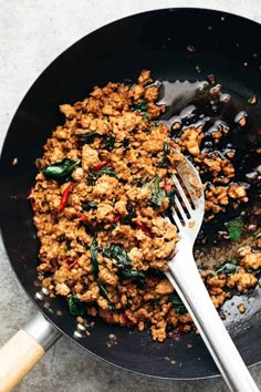 a skillet filled with meat and vegetables on top of a table next to a wooden spoon