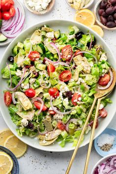 a salad in a white bowl with lemons, olives, tomatoes, onions and feta cheese