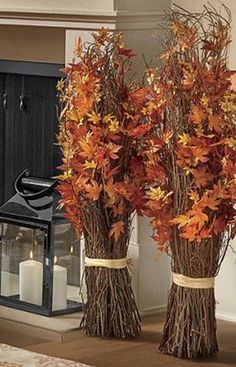 two tall vases filled with leaves next to a candle on the floor in front of a fireplace