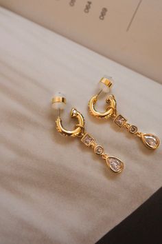 This pair of huggies with a hanging, bezel-set stones charm is the perfect accessory to dress up any outfit! Available in silver and gold. Details Sold as a pair Charm is removable 11mm x 2.5mm x 31mm 1.65 grams per earring Made from Brass with CZ Stones Posts are made from surgical steel so they are very hypo-allergenic for sensitive ears Earrings are 100% nickel-free and cadmium-free Limited Return Policy: LUV AJ is limited to a 7-day return period. For hygienic purposes, product must be in or Sensitive Ears Earrings, American Threads, Luv Aj, Sensitive Ears, Cz Stone, Gold Details, Bezel Setting, Gold And Silver, Trendy Fashion