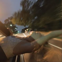 a person riding in the back of a car on a road at night with trees and street lights