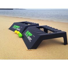 two black benches sitting on top of a sandy beach next to the ocean with tennis balls